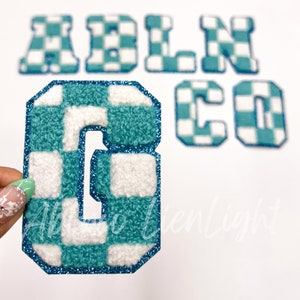 May include: Checkered blue and white felt letters spelling out the name "ADLNCO". The letters are outlined in blue glitter.