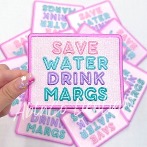 May include: A set of pink and white iron-on patches with the text "Save Water Drink Margs" in colorful, outlined letters. The patches are perfect for adding a fun and quirky touch to clothing, bags, or other accessories.