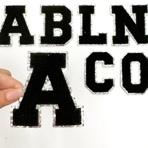 May include: Black felt letters with a silver glitter trim. The letters spell out "ABLNA CO".