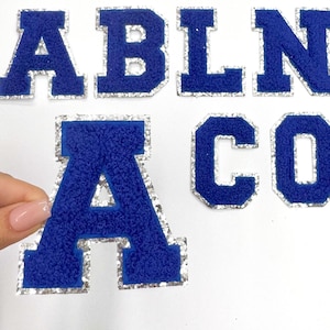 May include: A set of blue felt letters with silver glitter trim. The letters spell out "ABLNA CO".