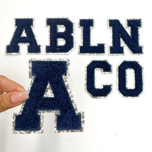May include: A set of navy blue felt letters with silver glitter trim. The letters spell out "ABLNACO".