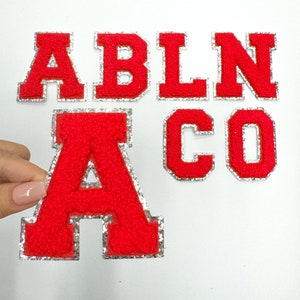 May include: Red felt letters with a silver outline spelling out "ABLNACO".