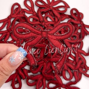 May include: A pile of red felt fabric bows. The bows are about 2 inches wide and have a simple, classic design.