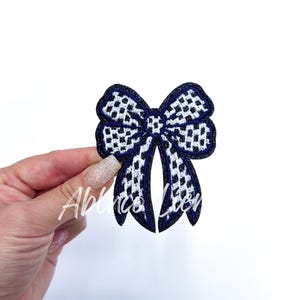 May include: A blue and white checkered bow with a glittery finish. The bow is made of fabric and has a stitched edge.