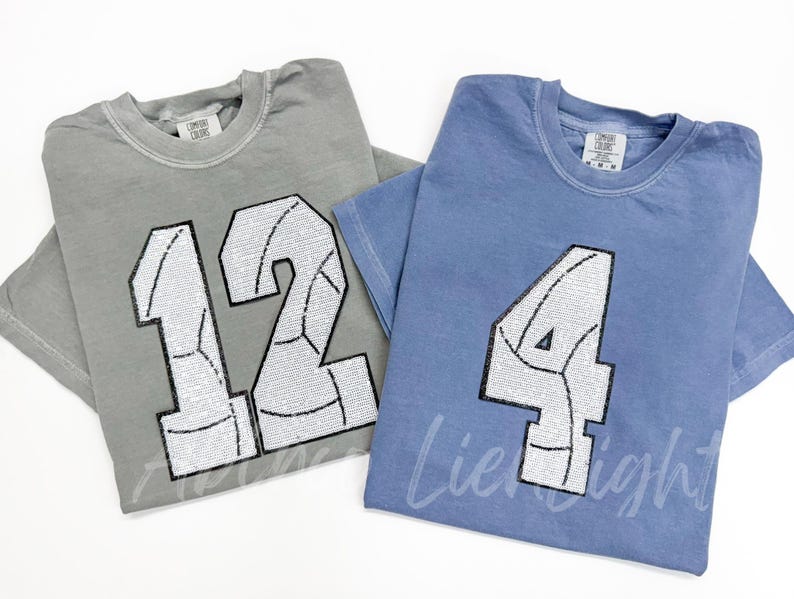 K&ouml;nnte beinhalten: Zwei T-Shirts mit Paillettenzahlen und einem Volleyball-Design. Das Shirt links ist grau mit der Nummer 12. Das Shirt rechts ist blau mit der Nummer 4.