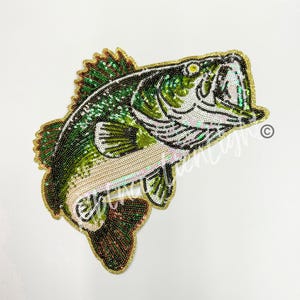 May include: A green and gold sequined bass fish patch. The fish is in a jumping position with its mouth open. The patch is perfect for adding a touch of whimsy to clothing, bags, or other crafts.