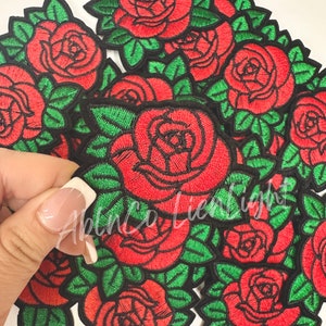 May include: A pile of red embroidered rose patches with green leaves. The patches are on a white background.