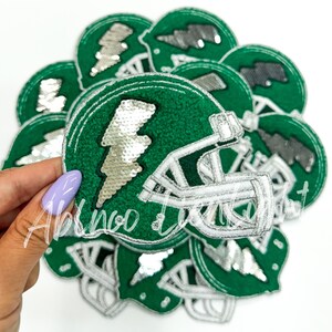 May include: A stack of green and white felt patches with a silver sequin lightning bolt and a white football helmet design.