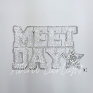 May include: Silver glitter iron-on patch with the words "Meet Day" and a silver glitter star.