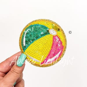 May include: A round, colorful, sequined beach ball patch with a yellow, green, pink, and white design.
