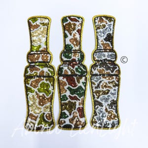 May include: Three gold-trimmed fabric patches in a camouflage pattern. The patches are shaped like a bottle and are decorated with sequins.