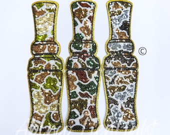 May include: Three gold-trimmed fabric patches in a camouflage pattern. The patches are shaped like a bottle and are decorated with sequins.