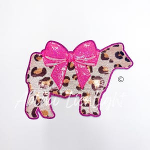 May include: A pink sequined bow on a brown and white leopard print cow applique.