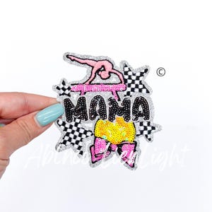 May include: A silver sequin patch with a pink gymnast on a pink balance beam, a black and white checkered star, a yellow and pink bow, and the word "MAMA" in black sequins.