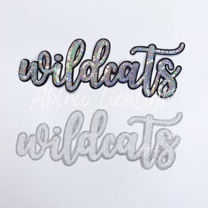 May include: Two versions of the word "Wildcats" in a cursive font, one with iridescent sequins and one with silver sequins.