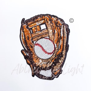 May include: A brown and orange sequined baseball glove with a white baseball inside. The glove is decorated with sequins and has a black outline.