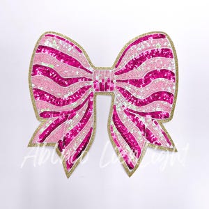 May include: Pink and white striped sequin bow with a gold outline. The bow is a fabric applique.