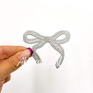 May include: A silver glitter bow with a loop on the top. The bow is about 2 inches wide.