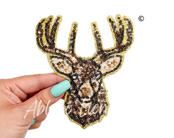May include: A gold and brown sequined deer head applique patch. The deer has large antlers and a detailed face.