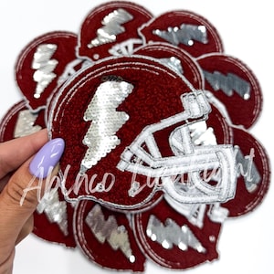 May include: A stack of red and white felt iron-on patches featuring a football helmet with a silver sequined lightning bolt.