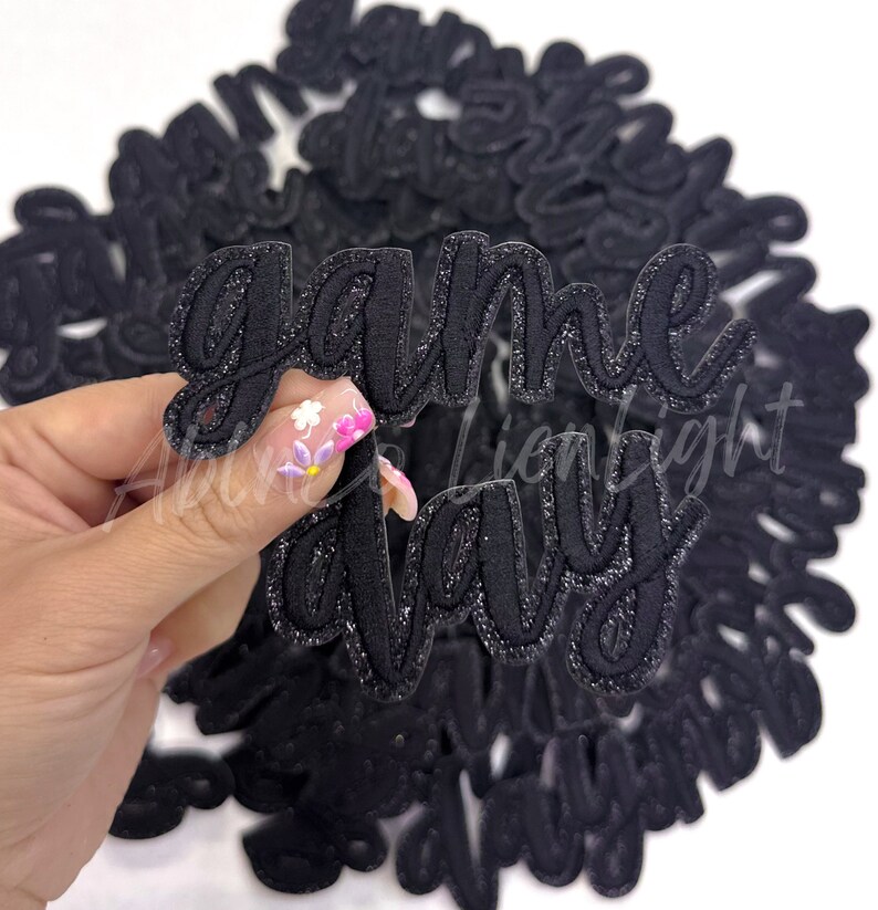 Puede incluir: Un mont&oacute;n de parches de planchado de brillo negro que dicen "game day" en una fuente cursiva.