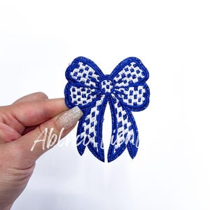 May include: A blue and white checkered bow with a glittery finish. The bow is made of fabric and has a slightly raised texture.