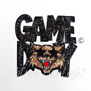 May include: Black sequined "GAME DAY" patch featuring a snarling panther with gold and red accents. The patch is designed with a bold, eye-catching font and a copyright symbol.
