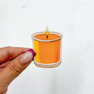 May include: A yellow and white embroidered iron-on patch of a candle with a flame.