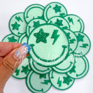 May include: A set of 10 green iron-on patches featuring a smiling face with a lightning bolt and a glitter star.