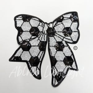 May include: A black and white sequined bow with a soccer ball pattern. The bow is large and has a slightly ruffled texture.
