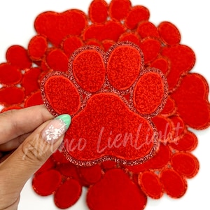 May include: A set of red felt paw print patches with a glittery outline. The paw prints are various sizes and are arranged in a circle.