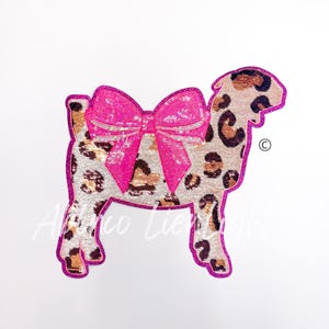 May include: A pink and gold sequined goat with a pink bow. The goat is a patch or applique.