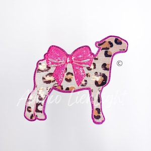 May include: A pink and brown sequined applique of a sheep with a large pink bow. The sheep is standing on all four legs and has a small tail. The applique is perfect for adding a touch of whimsy to any project.