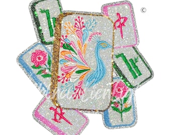 May include: A collection of sequined, rectangular accessories with embroidered designs. The central piece features a blue peacock with a colorful tail. Other pieces display floral and bamboo motifs, and Chinese characters. A gold chain is attached.