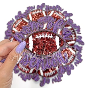May include: Purple and white iron-on patch with the text "Mom of a Senior" and a sequined football design.