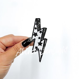 May include: Black and white lightning bolt patch with black star accents. The patch is made of sequins and is perfect for adding a touch of personality to clothing, bags, or other accessories.