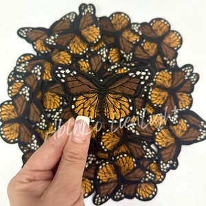 May include: A pile of brown and orange embroidered butterfly patches. The patches are about 2 inches wide and have a black outline. The butterflies have white spots on their wings.