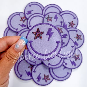 May include: A stack of purple iron-on patches with a smiley face, a lightning bolt, and a sparkly star.