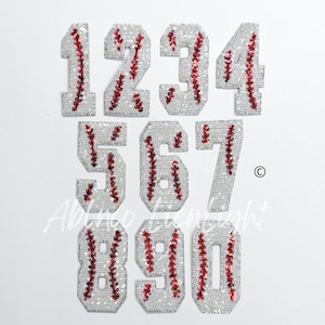 May include: Set of ten 3-inch iron-on patches featuring the numbers 1 through 10. Each number is white with red baseball stitching.