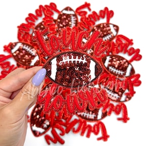 May include: A close-up of a pile of red and white iron-on patches with the word "Touchdown" and a sequined football design.