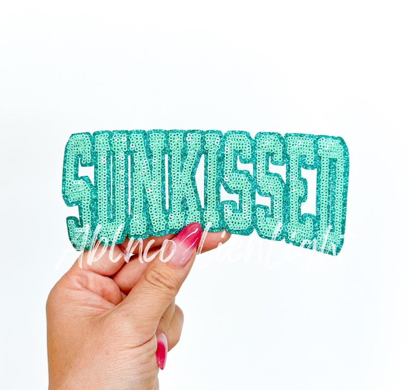 May include: A teal blue iron-on patch with the word "SUNKISSED" in large, glittery letters.