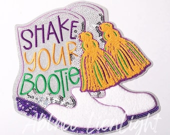 May include: White embroidered patch with a pair of white boots, gold tassels, and the text "Shake Your Bootie" in purple and green.