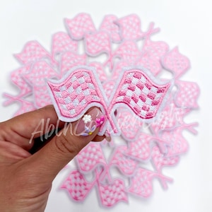 May include: A set of pink and white checkered racing flags. The flags are embroidered with a white checkered pattern on a pink background. The flags are perfect for adding a sporty touch to any project.