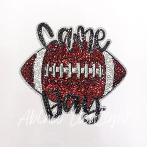 May include: A red and white football with silver sequins and the words "Game Day" in black sequins.