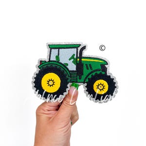 May include: Green and yellow tractor with silver glitter trim. The tractor is on a white background.