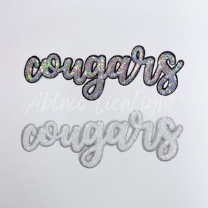 May include: Two iron-on patches with the word "cougars" in a cursive font. The top patch is silver with iridescent sequins. The bottom patch is white with white sequins.