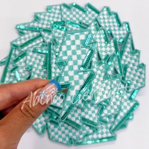 May include: A stack of green and white checkered lightning bolt patches with a sparkly green border. The patches are made of fabric and have a sewn-on design.
