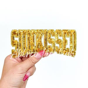 May include: Gold sequined iron-on patch that says "Slay" in all capital letters.