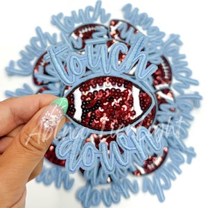 May include: A close-up of a blue felt patch with the words "touch down" and a red and white sequin football. The patch is surrounded by other similar patches.