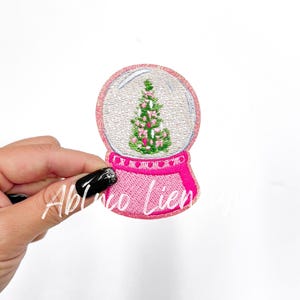 May include: Pink and white embroidered snow globe patch with a green Christmas tree inside.